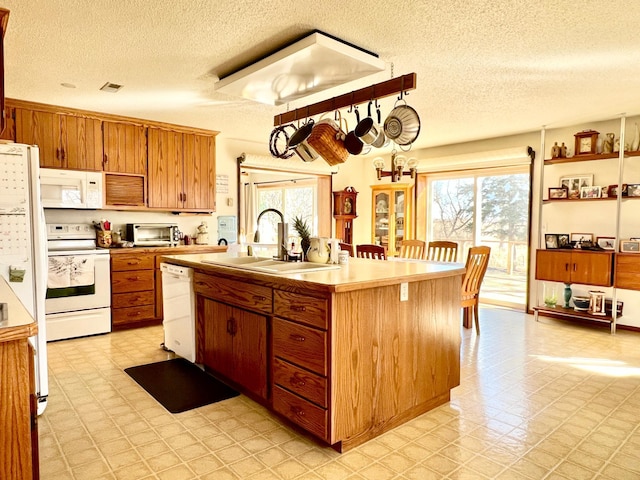 kitchen with white appliances, a sink, light countertops, light floors, and a center island with sink