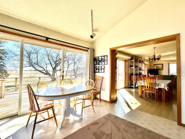 dining room featuring lofted ceiling, a textured ceiling, baseboards, rail lighting, and an inviting chandelier