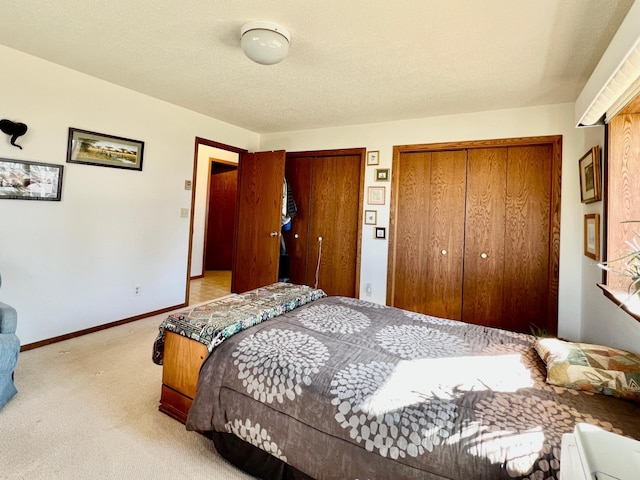 bedroom featuring multiple closets, light carpet, a textured ceiling, and baseboards