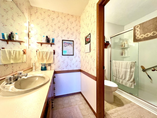 bathroom with wallpapered walls, a stall shower, baseboards, toilet, and vanity