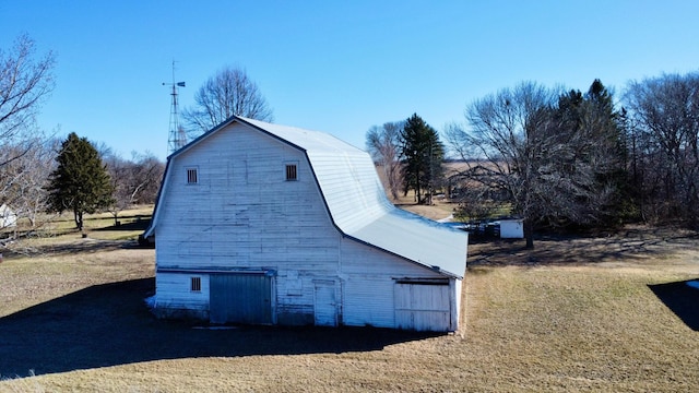 view of home's exterior with a garage, an outdoor structure, a barn, a gambrel roof, and a lawn