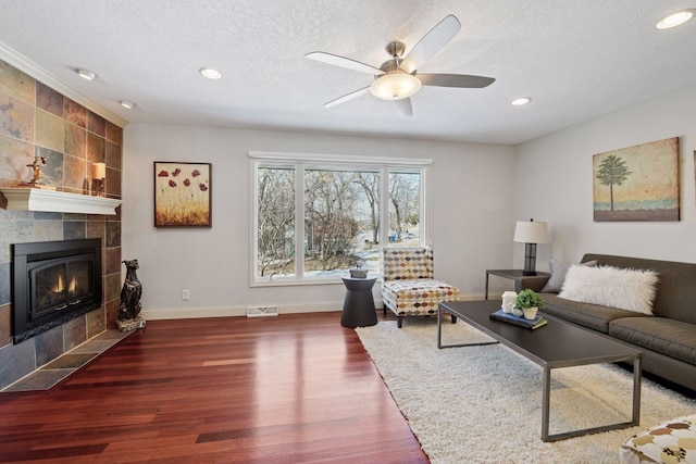 living area featuring wood finished floors, baseboards, visible vents, a tile fireplace, and a textured ceiling