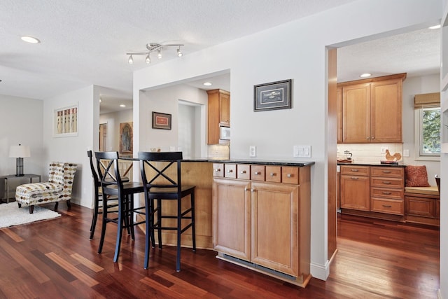 kitchen featuring dark countertops, backsplash, a breakfast bar area, dark wood-style floors, and a textured ceiling