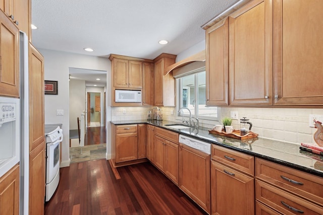 kitchen featuring white appliances, dark wood-style floors, dark stone counters, a sink, and tasteful backsplash