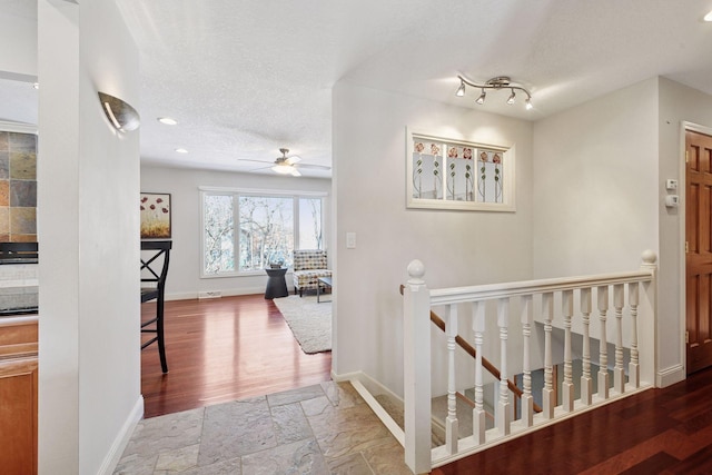 corridor with an upstairs landing, a textured ceiling, stone tile flooring, recessed lighting, and baseboards