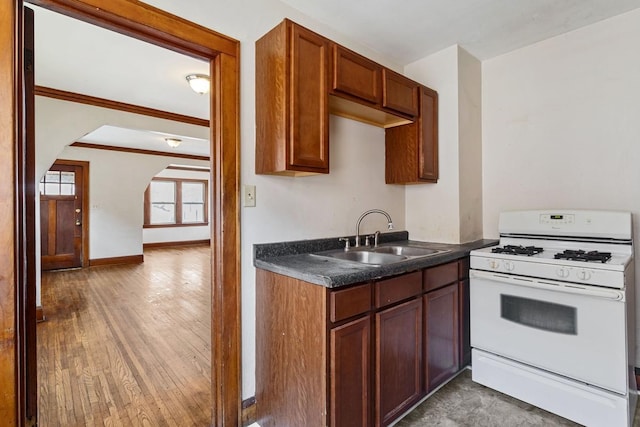 kitchen with dark countertops, white gas range oven, wood finished floors, arched walkways, and a sink