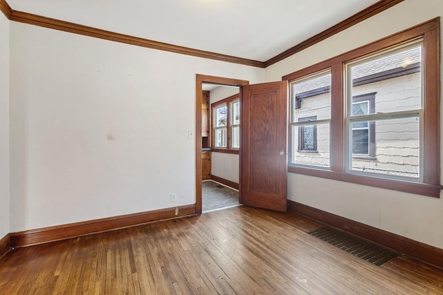 empty room with hardwood / wood-style floors, visible vents, baseboards, and ornamental molding