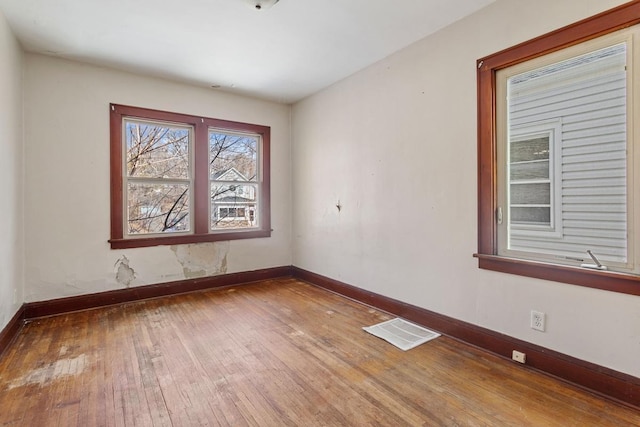 empty room with hardwood / wood-style floors, baseboards, and visible vents