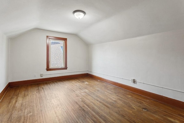 additional living space with baseboards, wood-type flooring, and vaulted ceiling