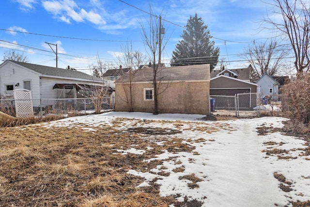 snow covered property featuring an outbuilding, a detached garage, and fence