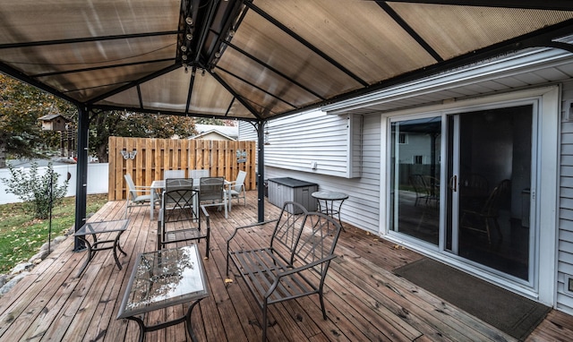 wooden terrace featuring a gazebo, outdoor dining area, and fence