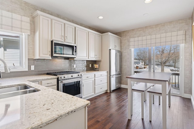 kitchen with a healthy amount of sunlight, appliances with stainless steel finishes, wallpapered walls, and a sink