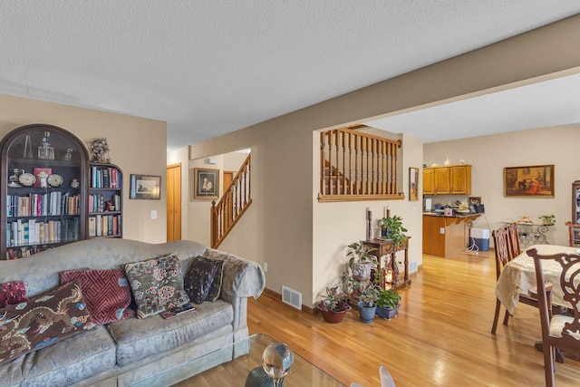 living area featuring light wood-style flooring, visible vents, stairway, and a textured ceiling