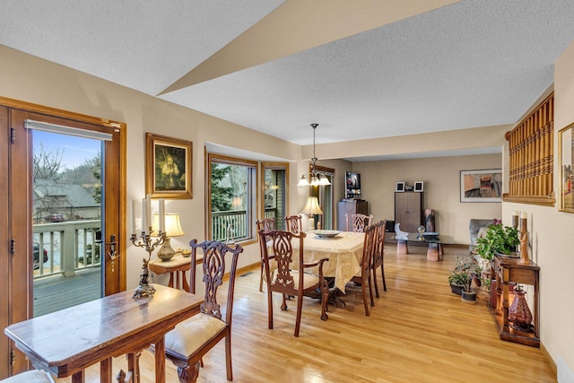 dining area with lofted ceiling, a healthy amount of sunlight, a textured ceiling, and light wood finished floors