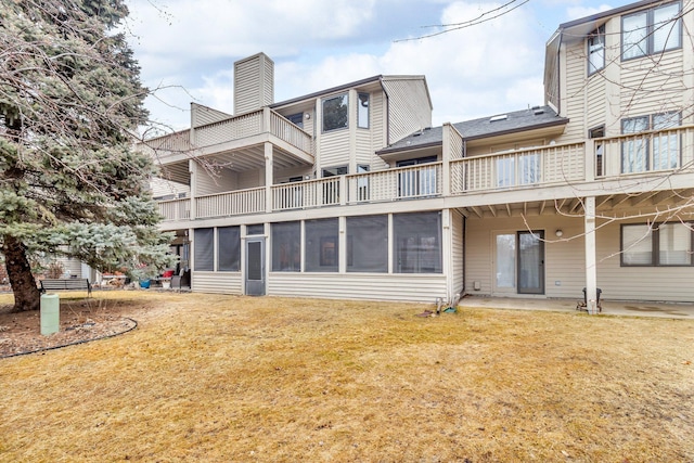 back of property with a balcony, a sunroom, a chimney, and a yard