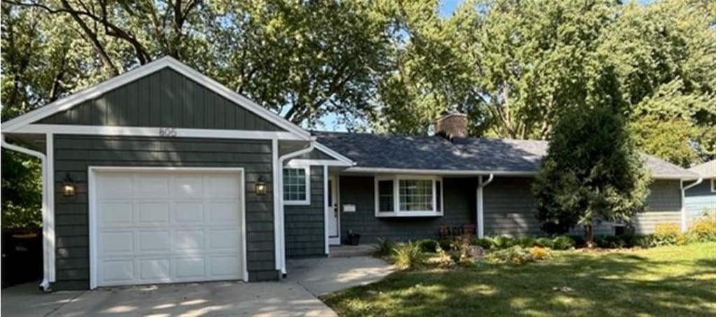 ranch-style home with driveway, a front lawn, a chimney, and an attached garage