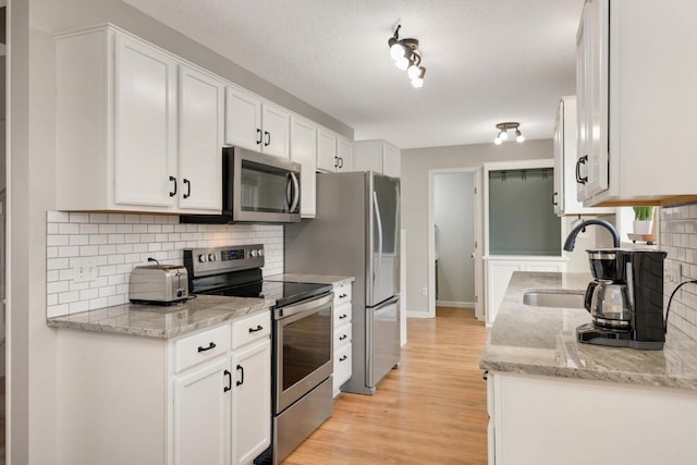 kitchen featuring a sink, stainless steel appliances, light wood-type flooring, white cabinetry, and backsplash