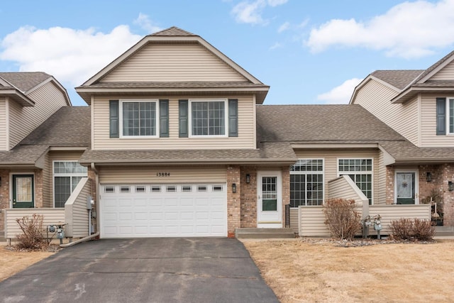 view of front of house featuring driveway, a shingled roof, an attached garage, and brick siding