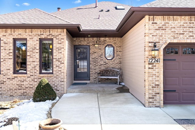 doorway to property featuring brick siding, an attached garage, and roof with shingles