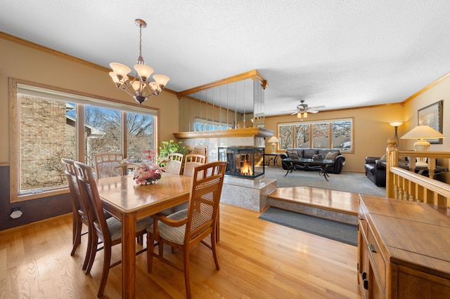 dining area featuring crown molding, a multi sided fireplace, and light wood finished floors