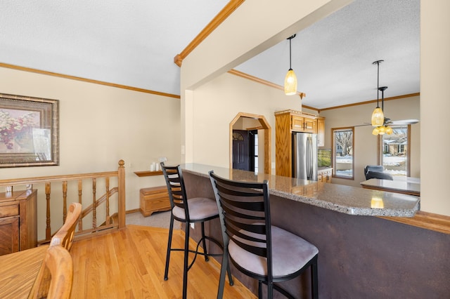 kitchen with baseboards, light wood finished floors, freestanding refrigerator, pendant lighting, and crown molding