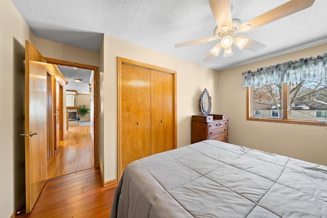 bedroom featuring a closet, wood-type flooring, a textured ceiling, and ceiling fan