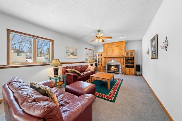 living area with baseboards, light carpet, a fireplace, a textured ceiling, and a ceiling fan