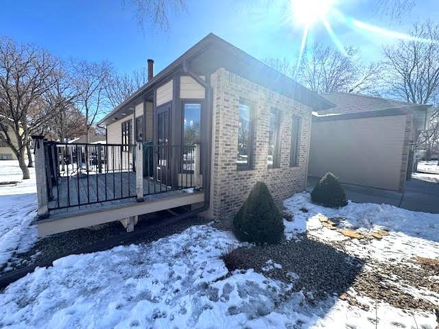 view of snowy exterior featuring a deck, an attached garage, and brick siding