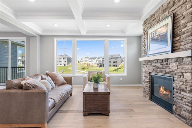 living room featuring light wood finished floors, a stone fireplace, crown molding, and baseboards