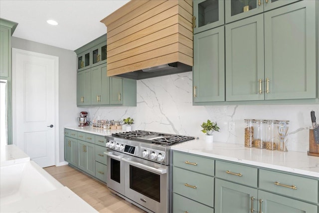 kitchen with light wood-style flooring, green cabinets, backsplash, custom exhaust hood, and double oven range