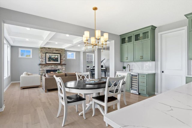 dining area with a stone fireplace, light wood-style flooring, beverage cooler, coffered ceiling, and beamed ceiling