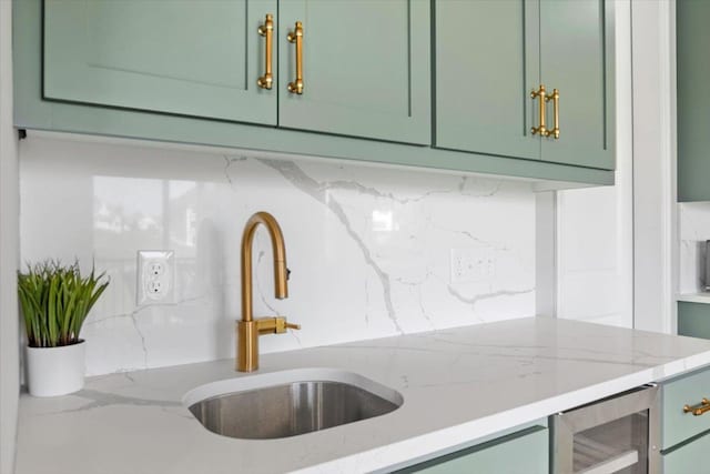 kitchen featuring wine cooler, a sink, green cabinets, backsplash, and light stone countertops