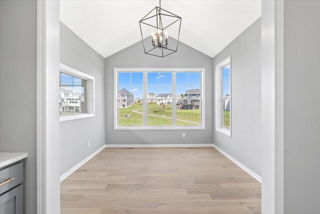 unfurnished dining area featuring lofted ceiling, baseboards, light wood finished floors, and an inviting chandelier