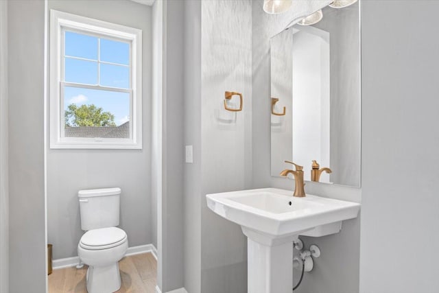 half bath with baseboards, toilet, and wood finished floors