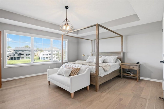 bedroom featuring light wood finished floors, a raised ceiling, visible vents, and baseboards