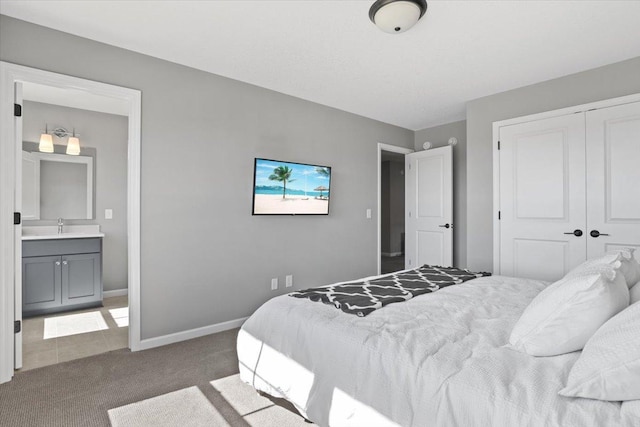 bedroom with a closet, baseboards, ensuite bath, carpet flooring, and a sink