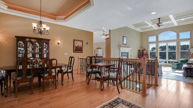 dining room featuring light wood-style flooring, ornamental molding, coffered ceiling, and a lit fireplace