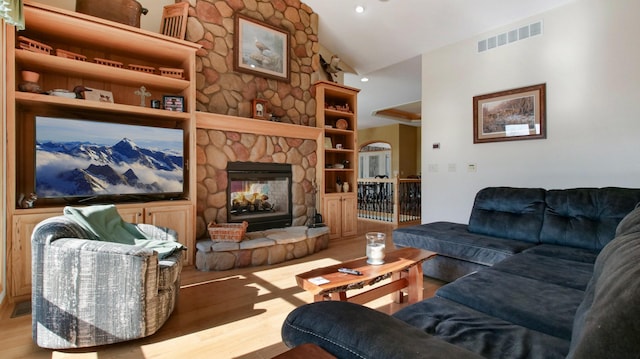 living room featuring lofted ceiling, visible vents, wood finished floors, and a stone fireplace