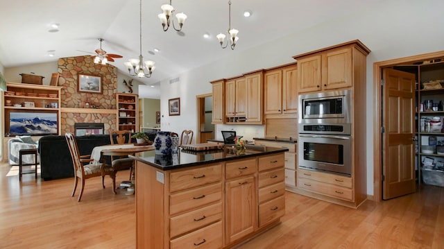 kitchen featuring a fireplace, a kitchen island, appliances with stainless steel finishes, light wood finished floors, and dark countertops