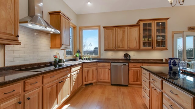 kitchen featuring light wood finished floors, dishwasher, black electric cooktop, wall chimney range hood, and a sink