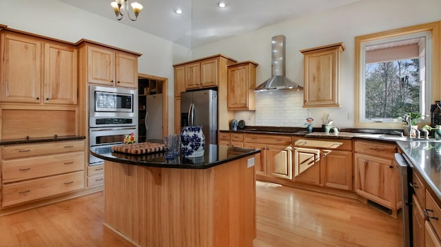 kitchen with a kitchen island, light wood-style floors, appliances with stainless steel finishes, backsplash, and wall chimney exhaust hood