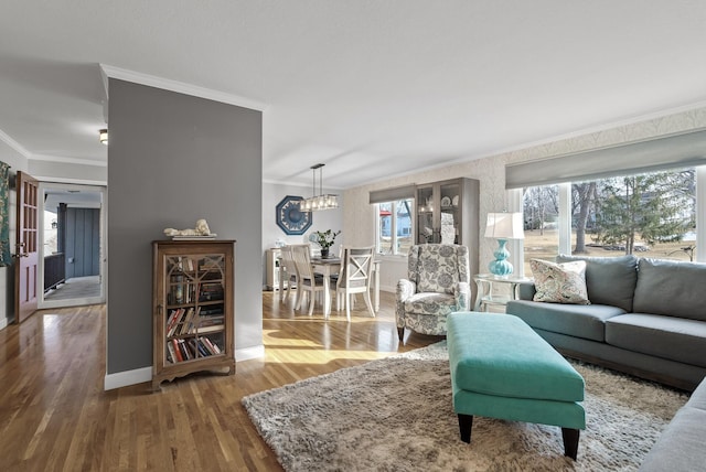 living area featuring baseboards, wood finished floors, a notable chandelier, and ornamental molding