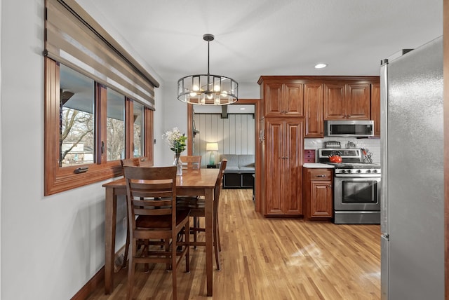 kitchen featuring hanging light fixtures, brown cabinets, light wood finished floors, and stainless steel appliances