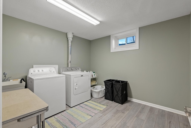 laundry area with a sink, a textured ceiling, light wood finished floors, baseboards, and washing machine and clothes dryer