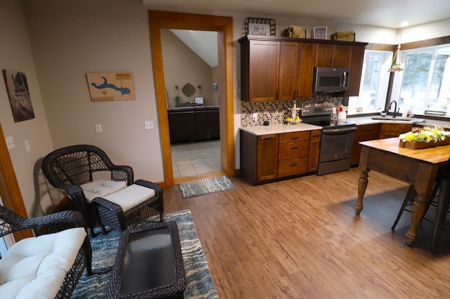 kitchen with light wood-style flooring, stainless steel microwave, light countertops, a sink, and range with electric stovetop