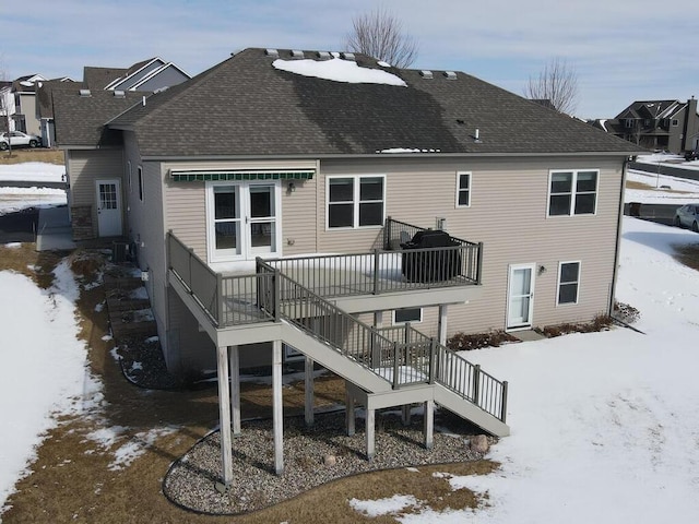 snow covered rear of property with stairway and a shingled roof