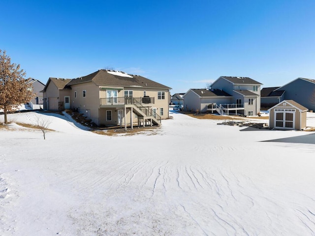 snow covered house featuring a storage unit, a residential view, an outbuilding, and stairs