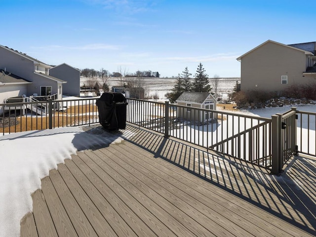 snow covered deck featuring a patio area, a shed, an outdoor structure, and area for grilling