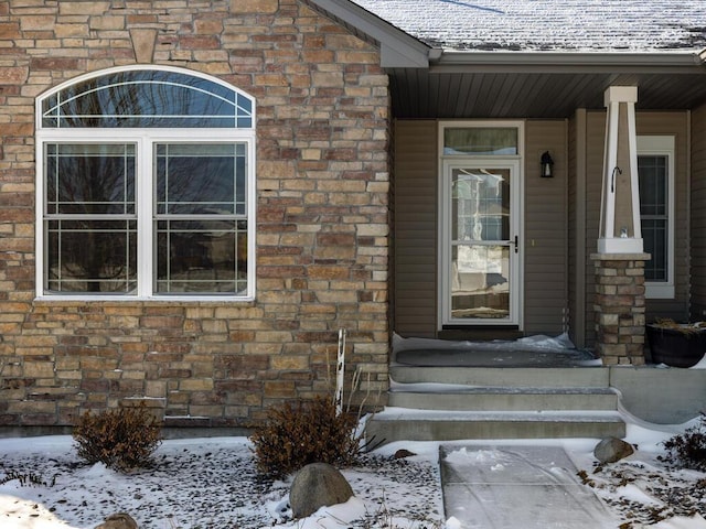 snow covered property entrance featuring stone siding and brick siding