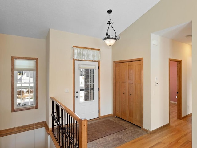 foyer entrance with light wood-style flooring, baseboards, and vaulted ceiling